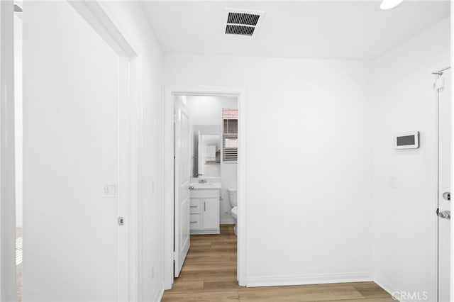 hallway featuring light wood finished floors, baseboards, and visible vents