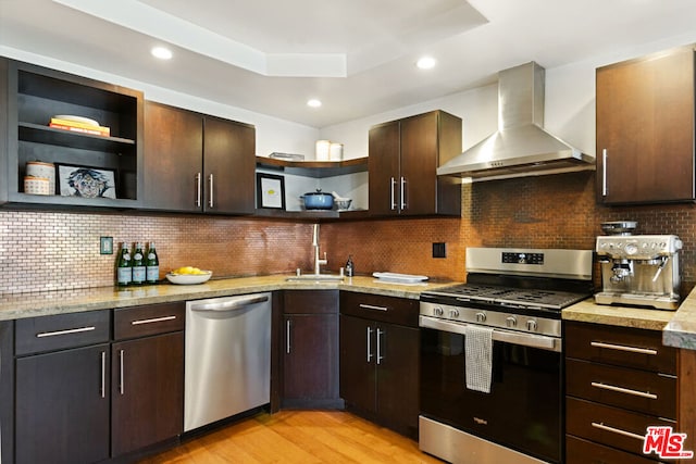 kitchen with wall chimney exhaust hood, stainless steel appliances, sink, backsplash, and light hardwood / wood-style flooring