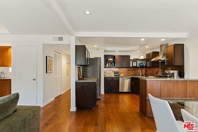 kitchen featuring wall chimney exhaust hood, dark hardwood / wood-style flooring, stainless steel appliances, backsplash, and kitchen peninsula