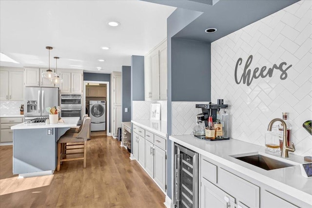 kitchen with washer / clothes dryer, sink, beverage cooler, hanging light fixtures, and stainless steel appliances