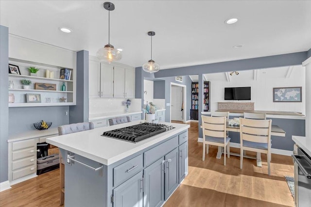 kitchen featuring gray cabinets, hanging light fixtures, a center island, stainless steel gas stovetop, and light wood-type flooring