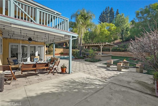 view of patio featuring ceiling fan, a balcony, french doors, and an outdoor living space with a fire pit