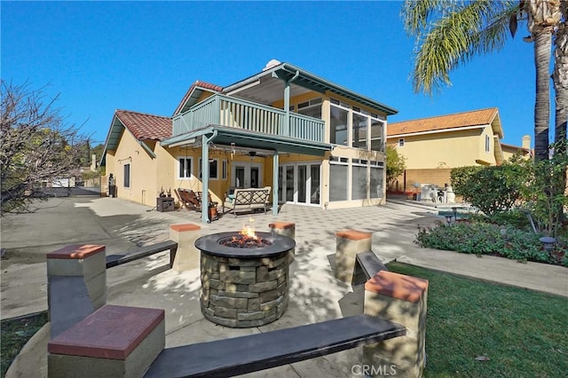 rear view of house with a balcony, a sunroom, a fire pit, and a patio