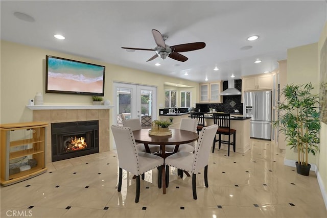 dining area featuring ceiling fan, light tile patterned floors, french doors, and a tile fireplace