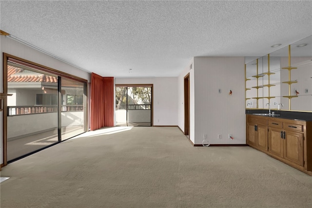 unfurnished living room with light carpet, a textured ceiling, and wet bar