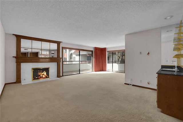 unfurnished living room featuring sink, light colored carpet, and a textured ceiling