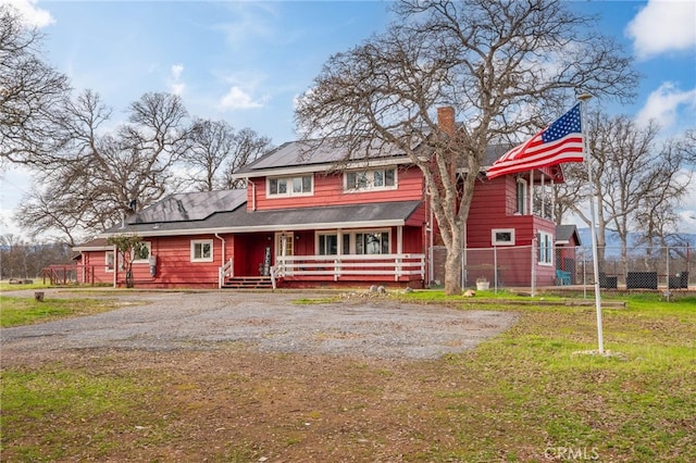 view of front of house featuring covered porch, a front lawn, and solar panels