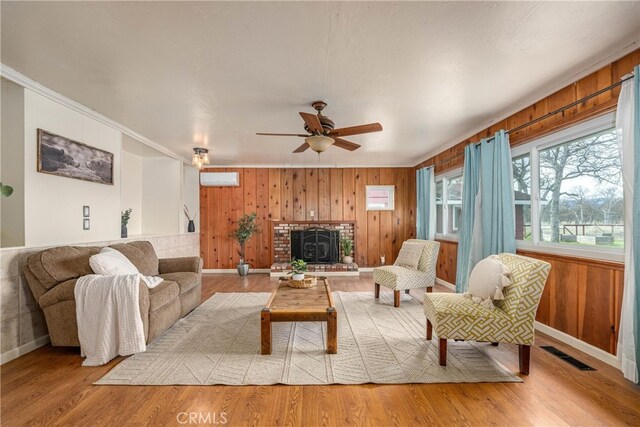 living room with a wall mounted AC, light wood-type flooring, wood walls, and ornamental molding