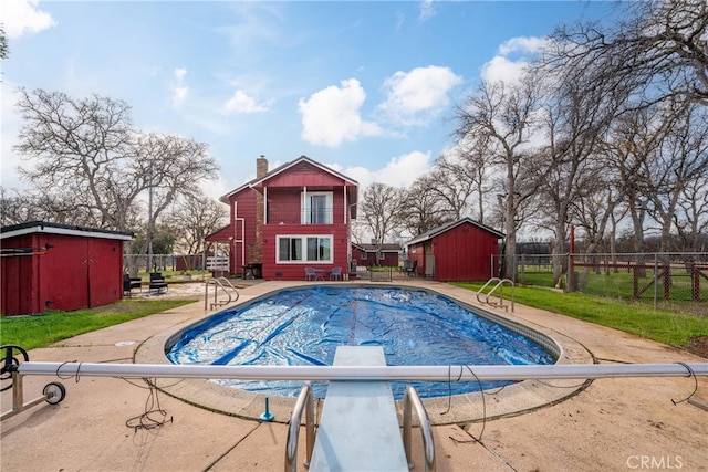 view of swimming pool featuring a storage shed and a diving board