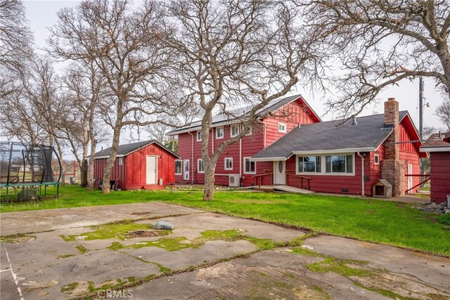 rear view of property featuring a storage unit, a lawn, and a trampoline