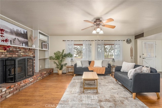 living room featuring ceiling fan, a fireplace, light hardwood / wood-style flooring, and a wall mounted air conditioner