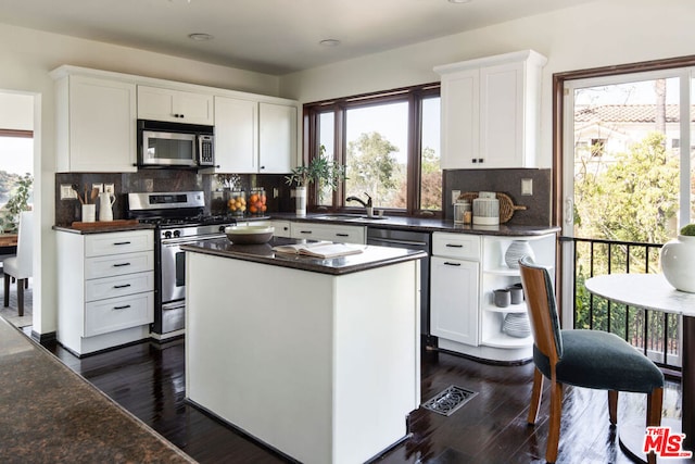 kitchen with appliances with stainless steel finishes, a kitchen island, dark wood-type flooring, white cabinetry, and sink