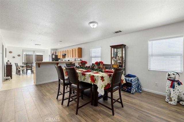 dining space with a textured ceiling, light wood-type flooring, and a healthy amount of sunlight