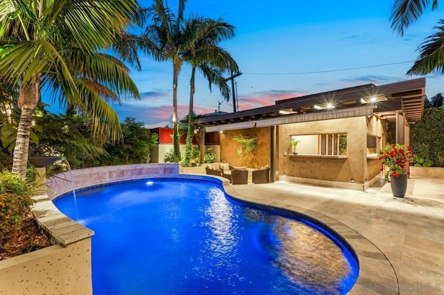 pool at dusk featuring pool water feature, an outdoor living space, and a patio area