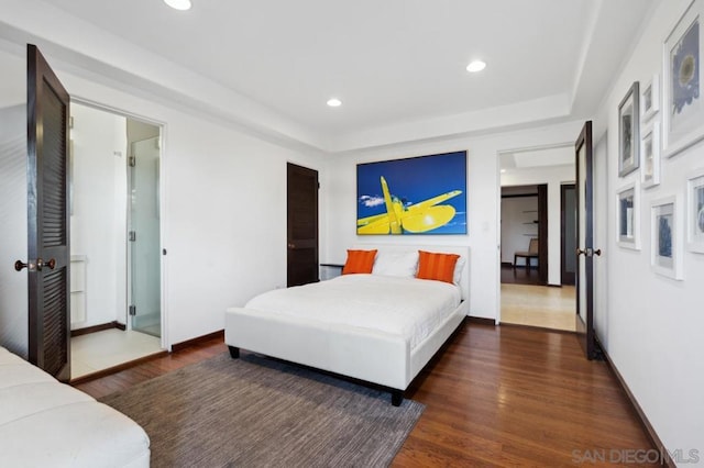 bedroom featuring a raised ceiling, dark hardwood / wood-style floors, and ensuite bath