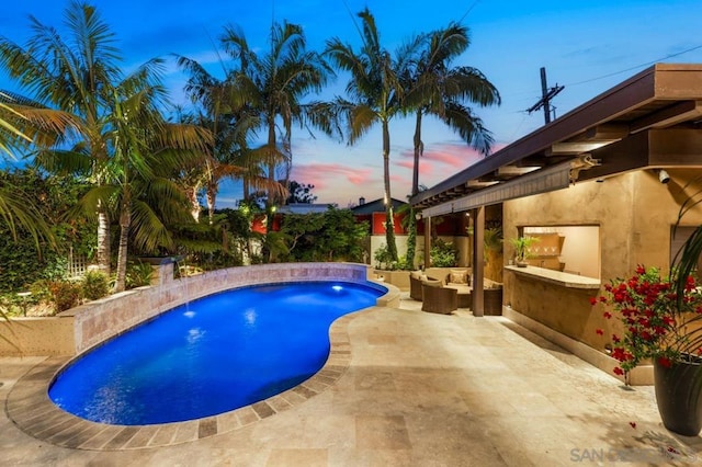 pool at dusk featuring a patio area, an outdoor hangout area, and pool water feature