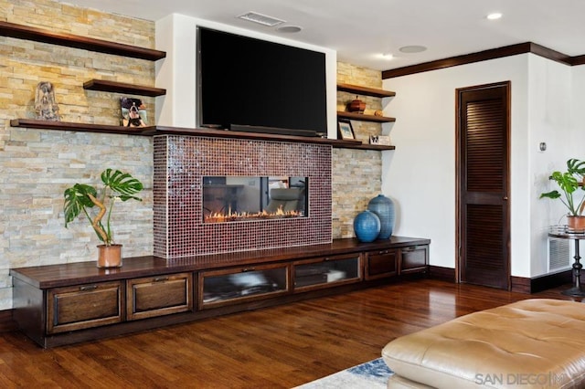 living room with dark wood-type flooring, a large fireplace, and crown molding