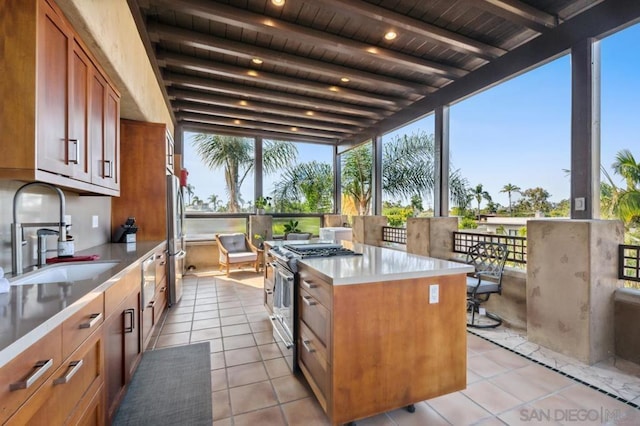 kitchen with a kitchen island, beamed ceiling, sink, appliances with stainless steel finishes, and light tile patterned floors