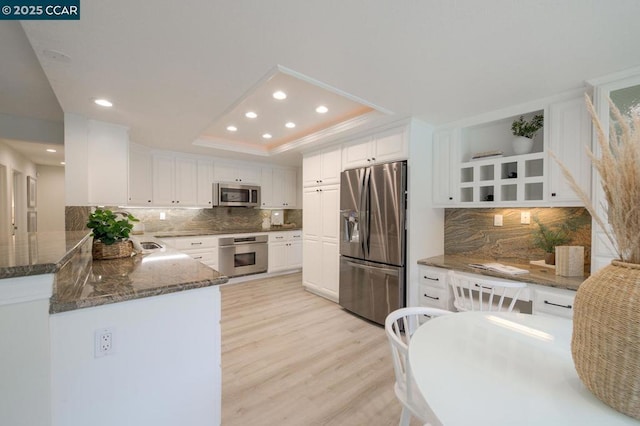 kitchen featuring a raised ceiling, dark stone countertops, white cabinets, kitchen peninsula, and stainless steel appliances