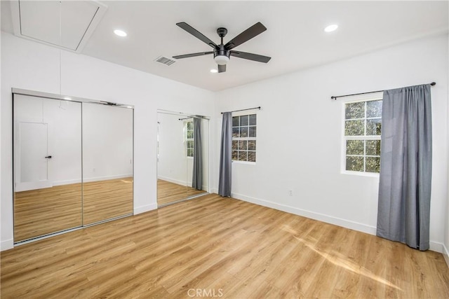 unfurnished bedroom with multiple windows, ceiling fan, light hardwood / wood-style flooring, and multiple closets