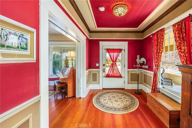 entryway with wood-type flooring, ornamental molding, and a tray ceiling