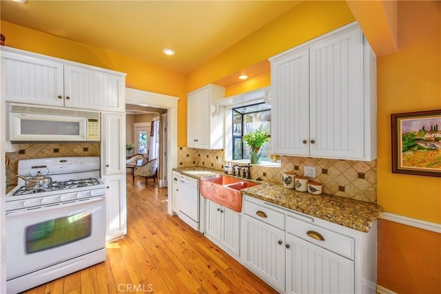 kitchen with dark stone countertops, backsplash, white cabinets, white appliances, and light wood-type flooring