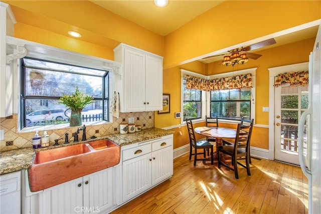 kitchen with sink, light hardwood / wood-style flooring, white cabinets, light stone countertops, and backsplash