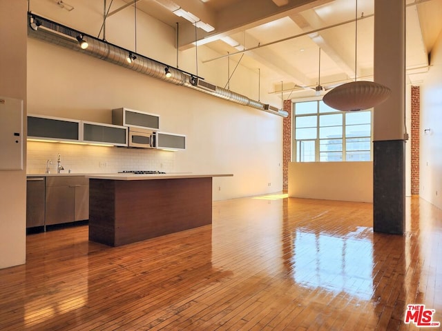 kitchen featuring hardwood / wood-style flooring, brick wall, a kitchen island, and a high ceiling