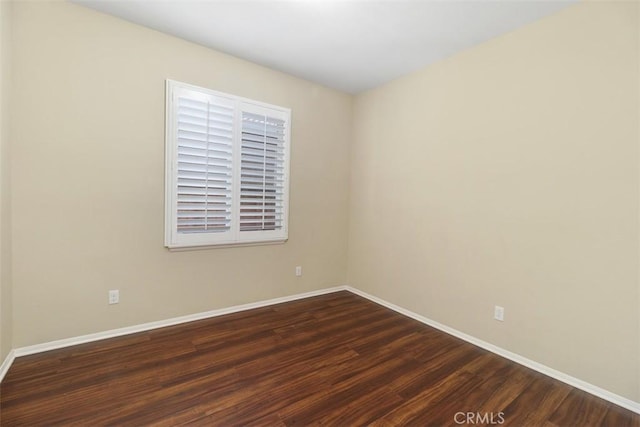 spare room featuring dark wood-type flooring and baseboards