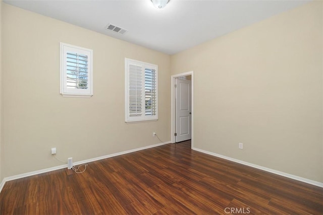 unfurnished room featuring dark wood-style floors, baseboards, and visible vents