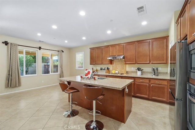 kitchen featuring brown cabinets, stainless steel appliances, visible vents, light stone countertops, and under cabinet range hood