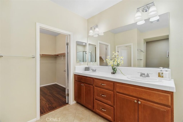 full bath featuring a sink, baseboards, tile patterned floors, double vanity, and a walk in closet