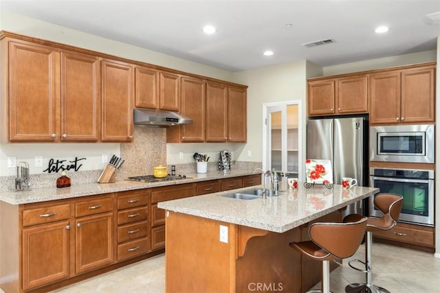 kitchen with visible vents, brown cabinetry, appliances with stainless steel finishes, under cabinet range hood, and a sink