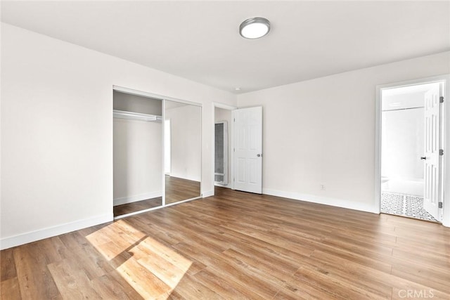 unfurnished bedroom with light wood-type flooring, a closet, and ensuite bathroom