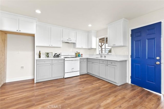 kitchen with white cabinets, gas range gas stove, sink, light wood-type flooring, and gray cabinetry