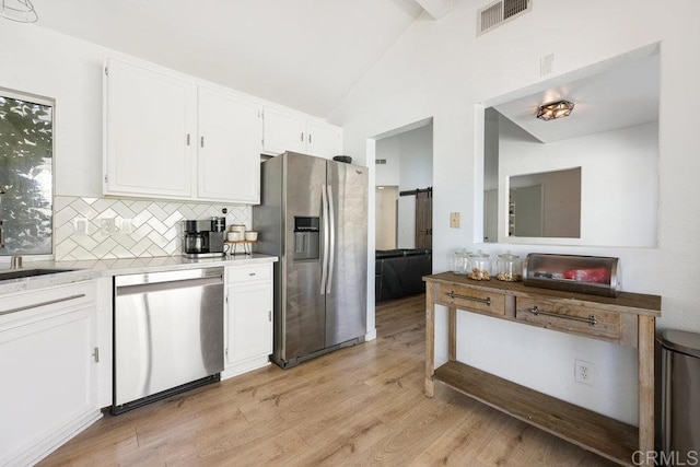 kitchen featuring vaulted ceiling, appliances with stainless steel finishes, white cabinets, decorative backsplash, and light hardwood / wood-style floors