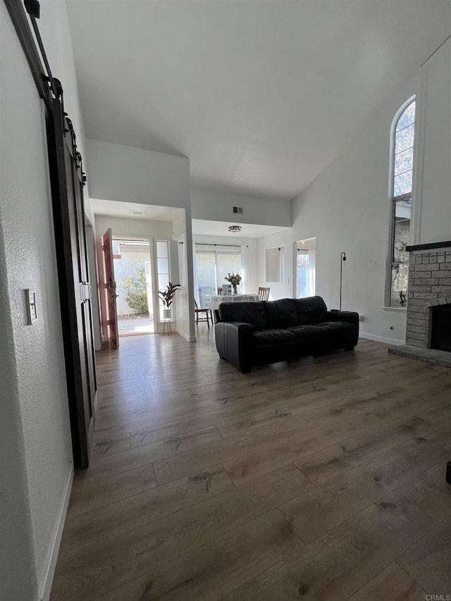 living room featuring dark hardwood / wood-style flooring, a stone fireplace, plenty of natural light, and a barn door