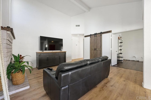 living room featuring a barn door, light wood-type flooring, high vaulted ceiling, and beam ceiling