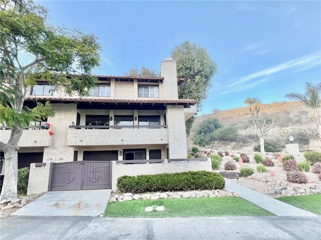 view of front of house featuring a balcony, a gate, stucco siding, a chimney, and a fenced front yard