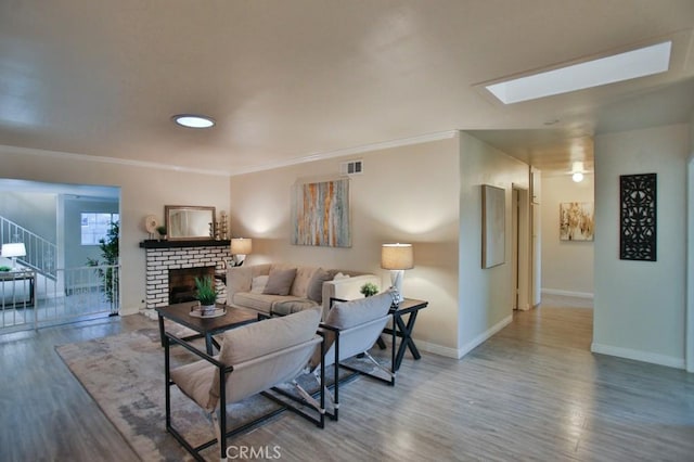 living room with hardwood / wood-style flooring, crown molding, a skylight, and a brick fireplace