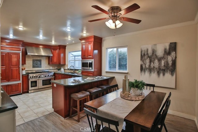 kitchen featuring wall chimney range hood, sink, backsplash, stainless steel appliances, and a kitchen bar