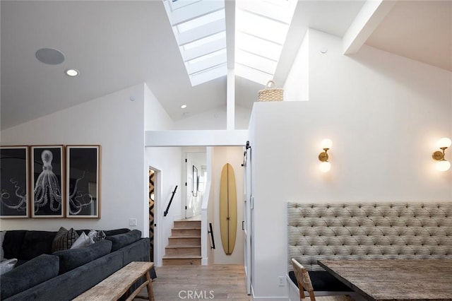 living room with light hardwood / wood-style floors, a barn door, and lofted ceiling with skylight