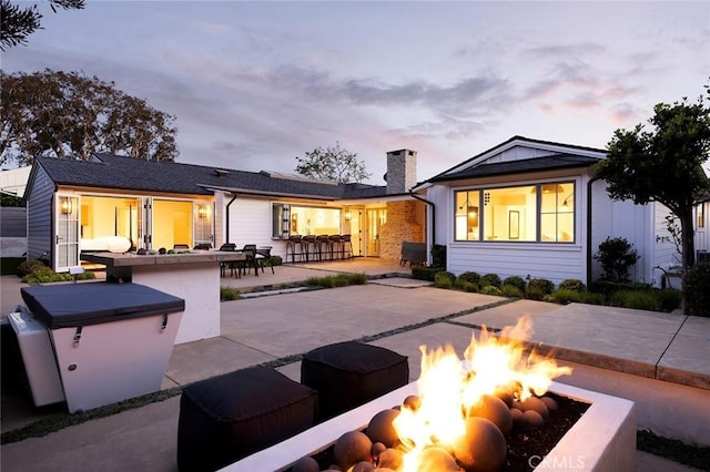 back house at dusk featuring an outdoor fire pit, a bar, and a patio area