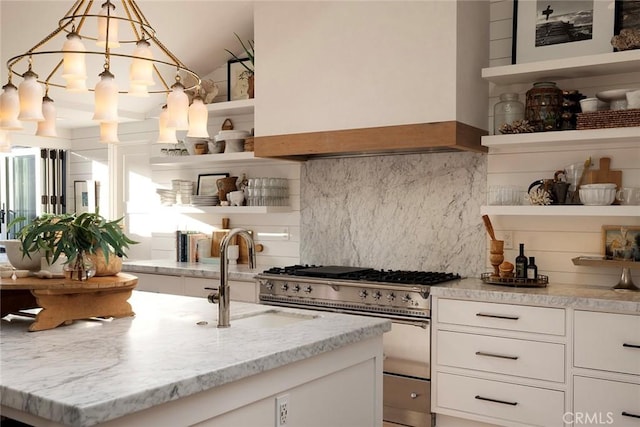 kitchen featuring light stone countertops, decorative light fixtures, white cabinetry, premium range hood, and sink