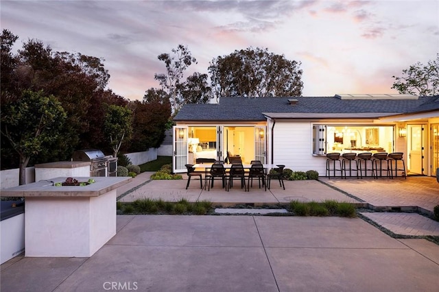 back house at dusk featuring exterior kitchen, a patio area, and a bar