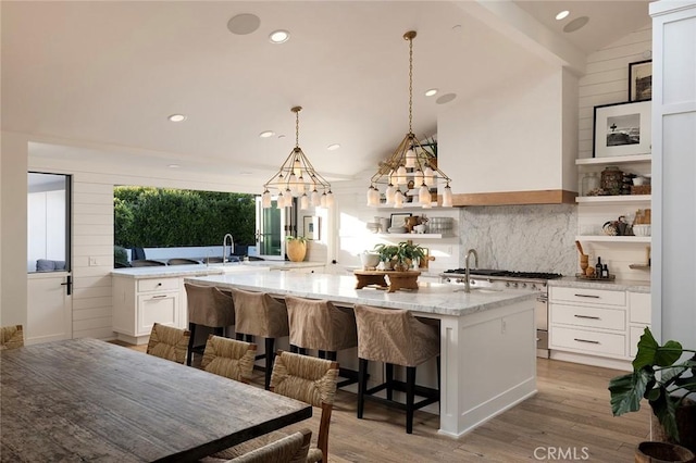 kitchen with vaulted ceiling, a kitchen island with sink, light stone countertops, a kitchen breakfast bar, and white cabinets