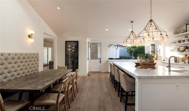 kitchen with a center island with sink, a kitchen bar, sink, hardwood / wood-style flooring, and hanging light fixtures