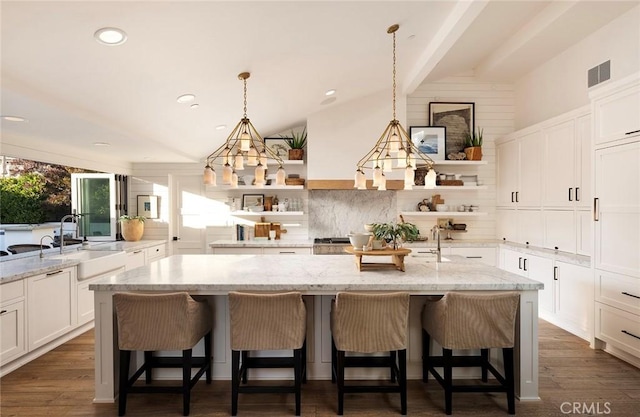 kitchen with a kitchen breakfast bar, sink, light stone counters, and an island with sink