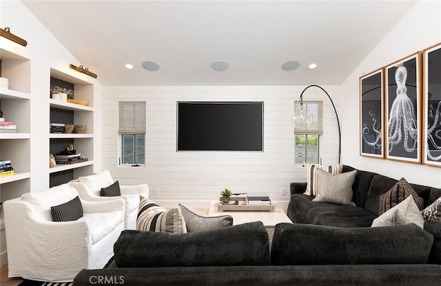 living room with built in features, wooden walls, and vaulted ceiling