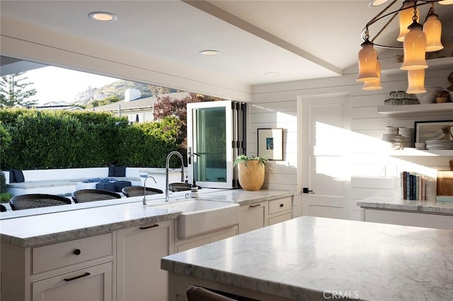 kitchen with light stone countertops, a center island, white cabinetry, sink, and hanging light fixtures